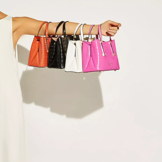 An arm holding out an orange, a black, a white and a pink handbag